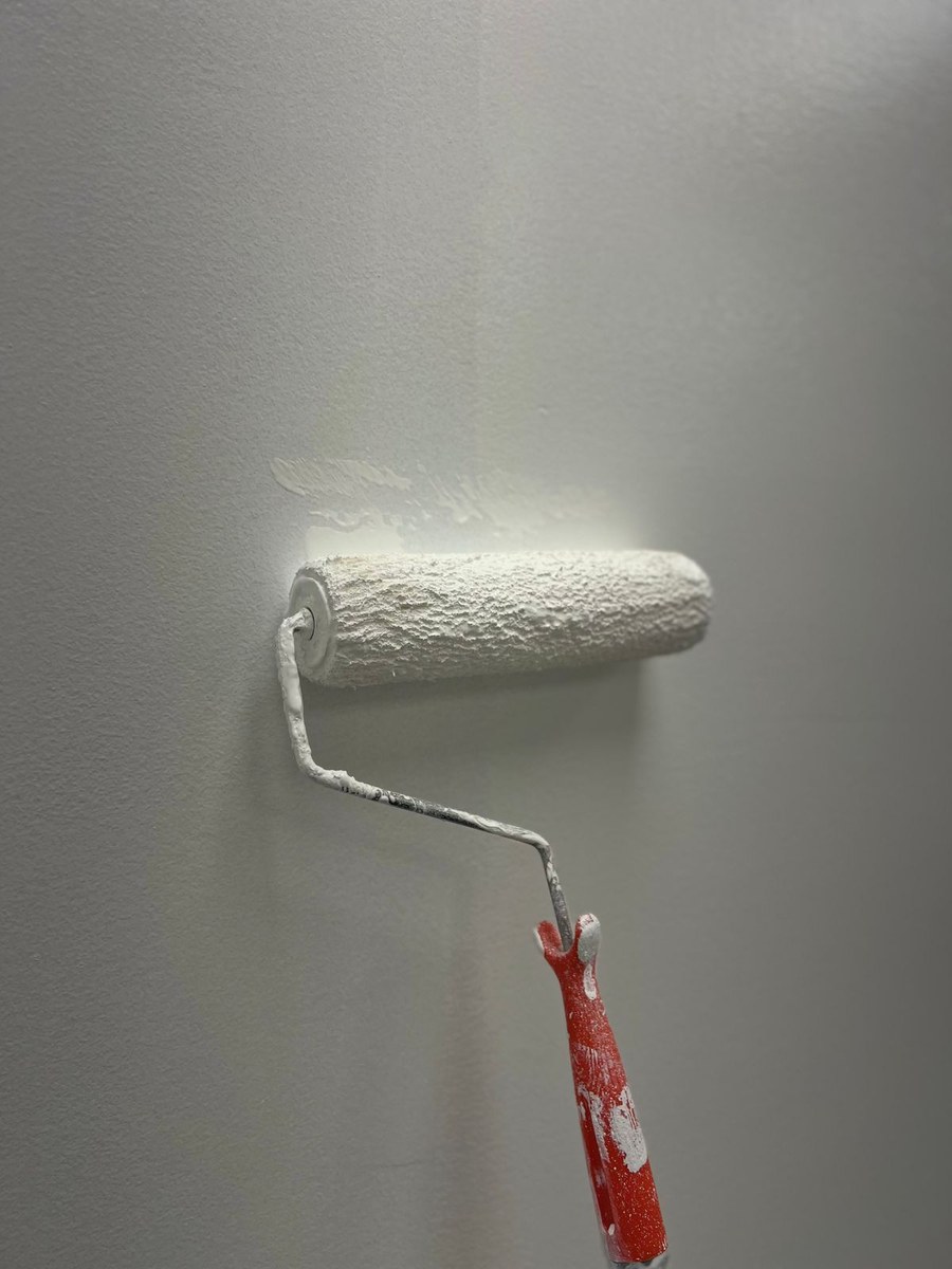 Close-up of a paint roller pressing against a textured wall surface